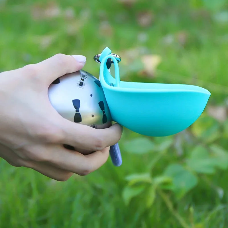 Close-up of a hand holding a teal portable dog water bottle with fold-out bowl outdoors